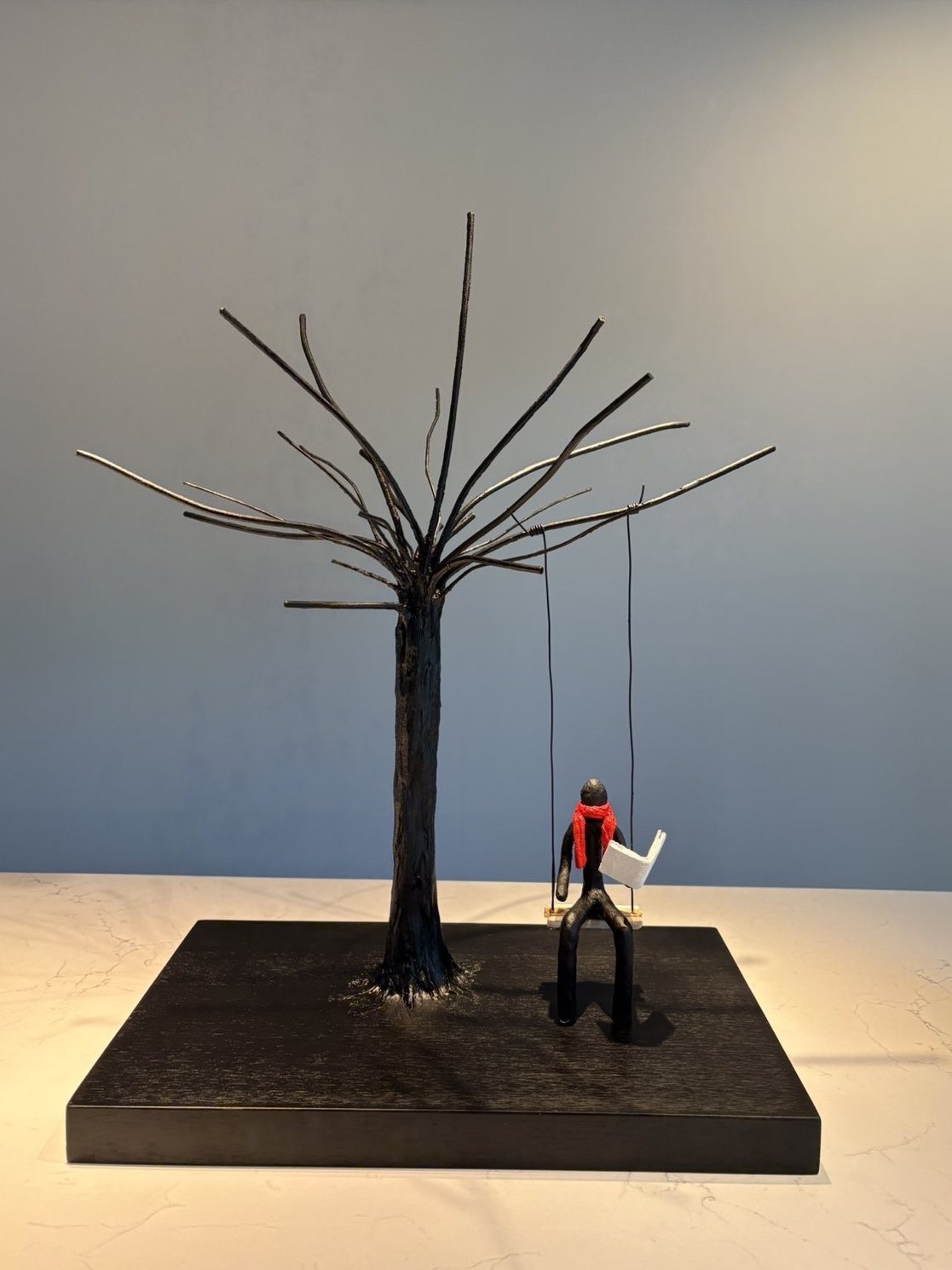 Arbre en métal et petit personnage à l’écharpe rouge lisant
