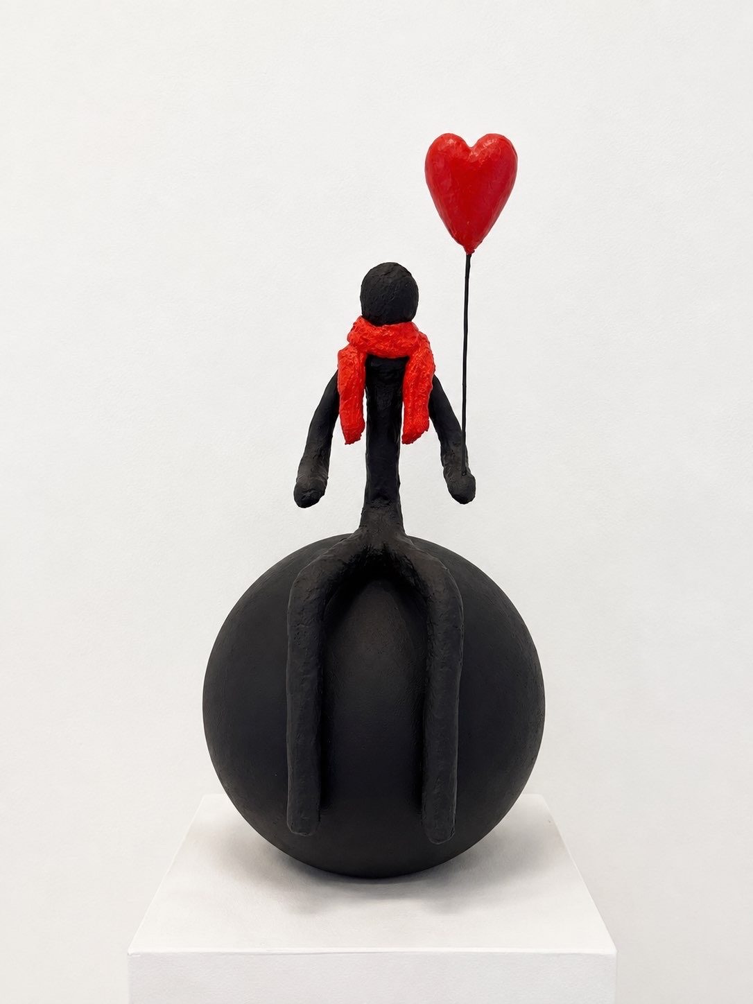 Personnage à l’écharpe rouge assis sur une sphère, ballon en forme de cœur